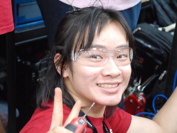 Team member in safety glasses working on the robot in the pits, giving a peace sign