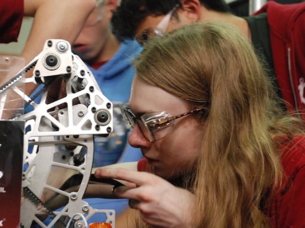 Student examining the robot's machined arm mechanism during a pit inspection