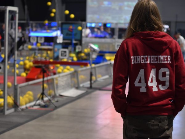 Team member in a personalized 449 hoodie watching a match at a large competition venue